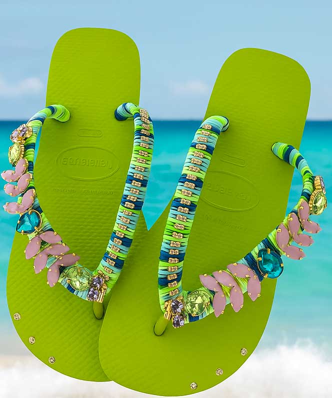 Sandalias verde lima con tiras turquesa, rosa y doradas, con océano y cielo azul de fondo.
