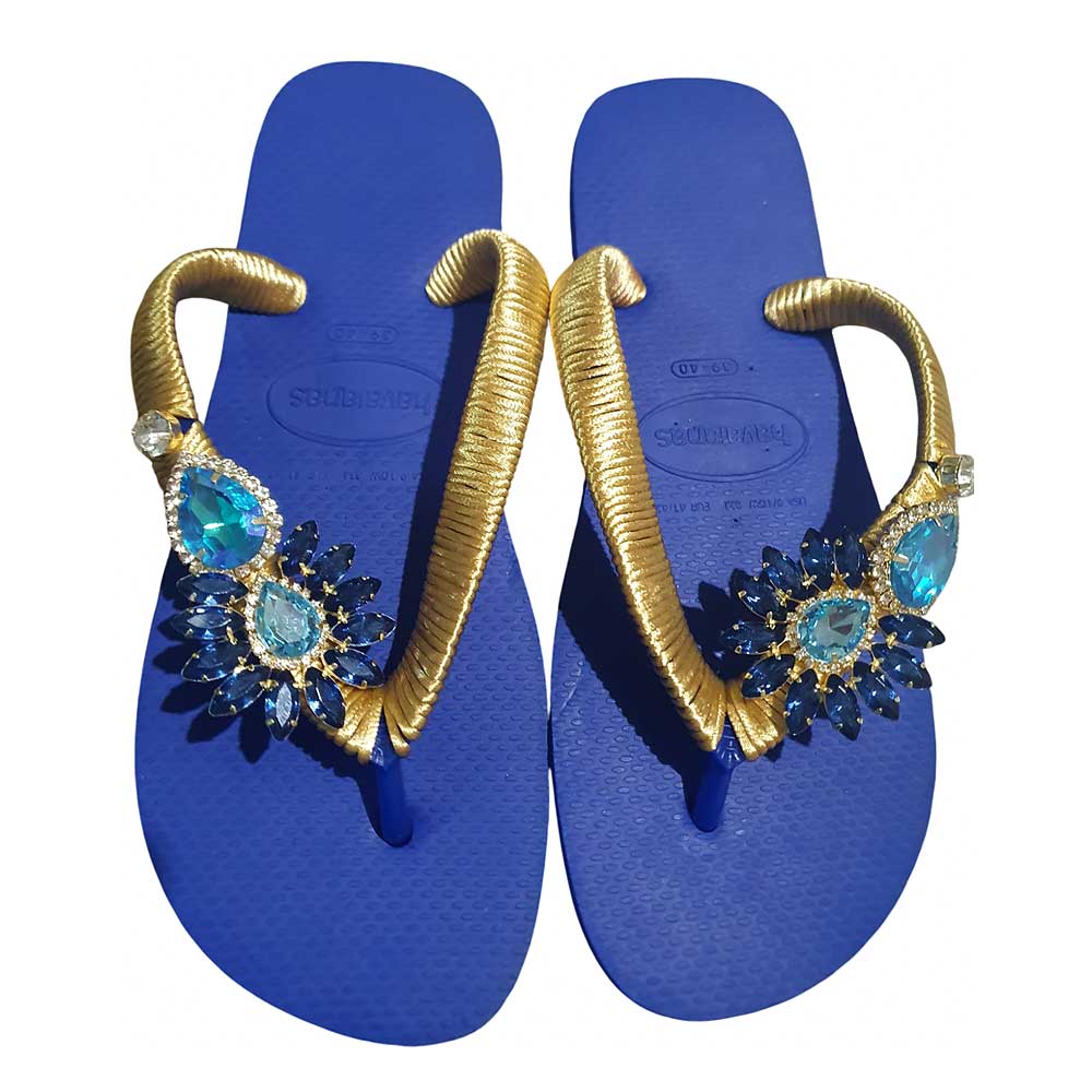 Chanclas Havaianas con tiras envueltas en cinta dorada y decoradas con pedrería en tonos azules.
