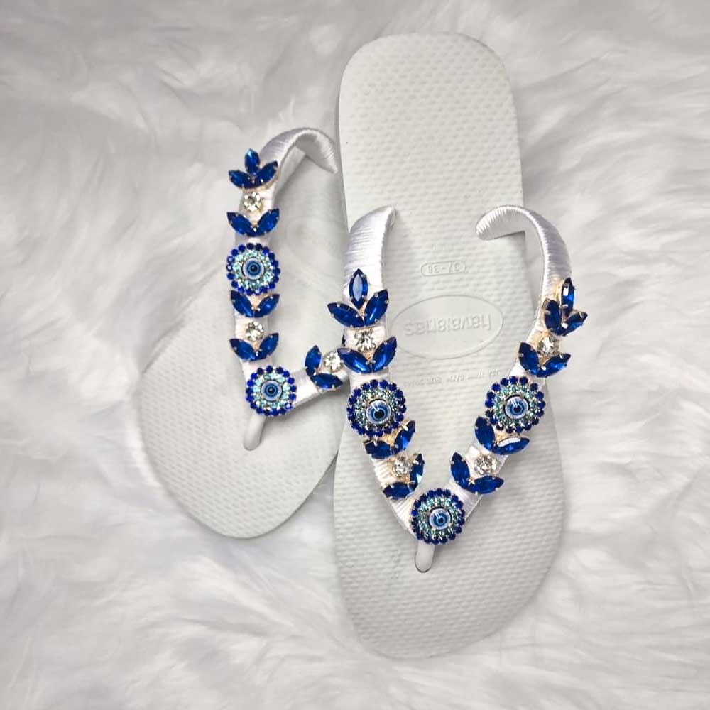 Chanclas Havaianas blancas con tiras decoradas con pedrería azul y flores de cristal.